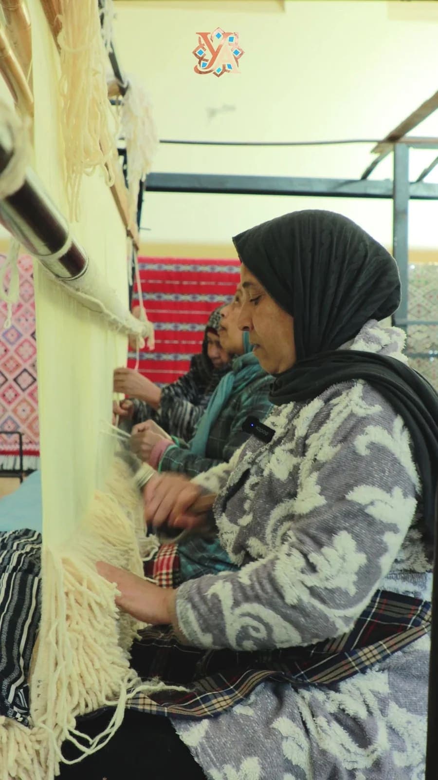 Une artisane travaille devant un métier à tisser vertical, avec d’autres femmes à ses côtés.