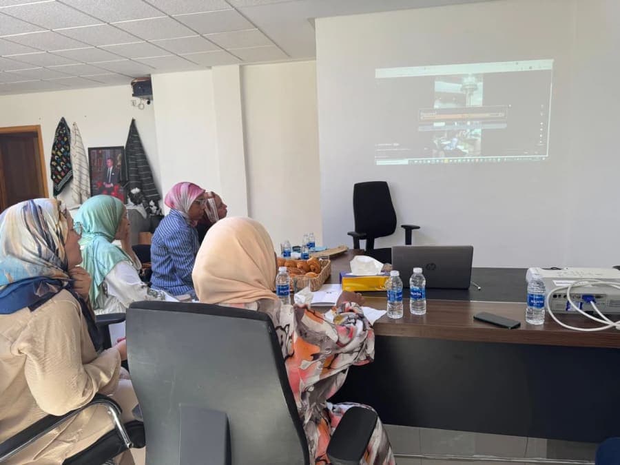 Des participantes regardent une démonstration projetée au mur, avec un ordinateur portable et un projecteur sur la table.