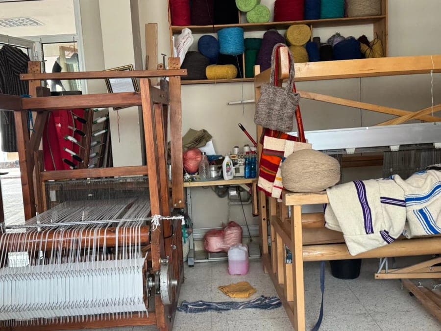 Un métier à tisser en bois, des fils et différents objets textiles occupent un atelier.